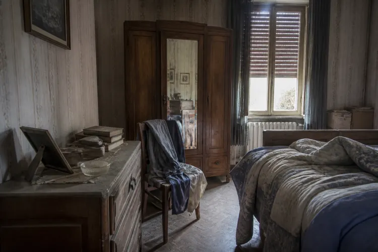 Une chambre restée fermée : volets tirés, poussière épaisse et effets personnels encore en place.
